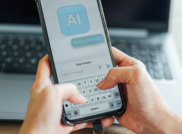 Close-up of hands typing on a smartphone showing an AI chat interface with the message 'Hi, may I help you?'